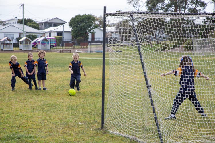 Students kicking goals in soccer net.